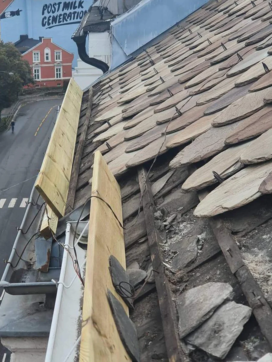 Skadet skifer og synlig underlag ved en takkant