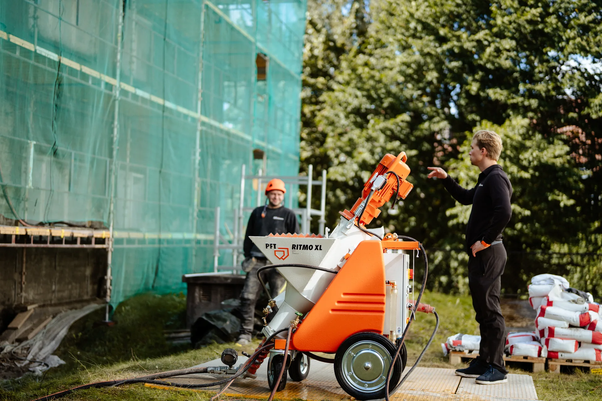 Medarbeidere og mørtelutstyr ved stillas på en byggeplass