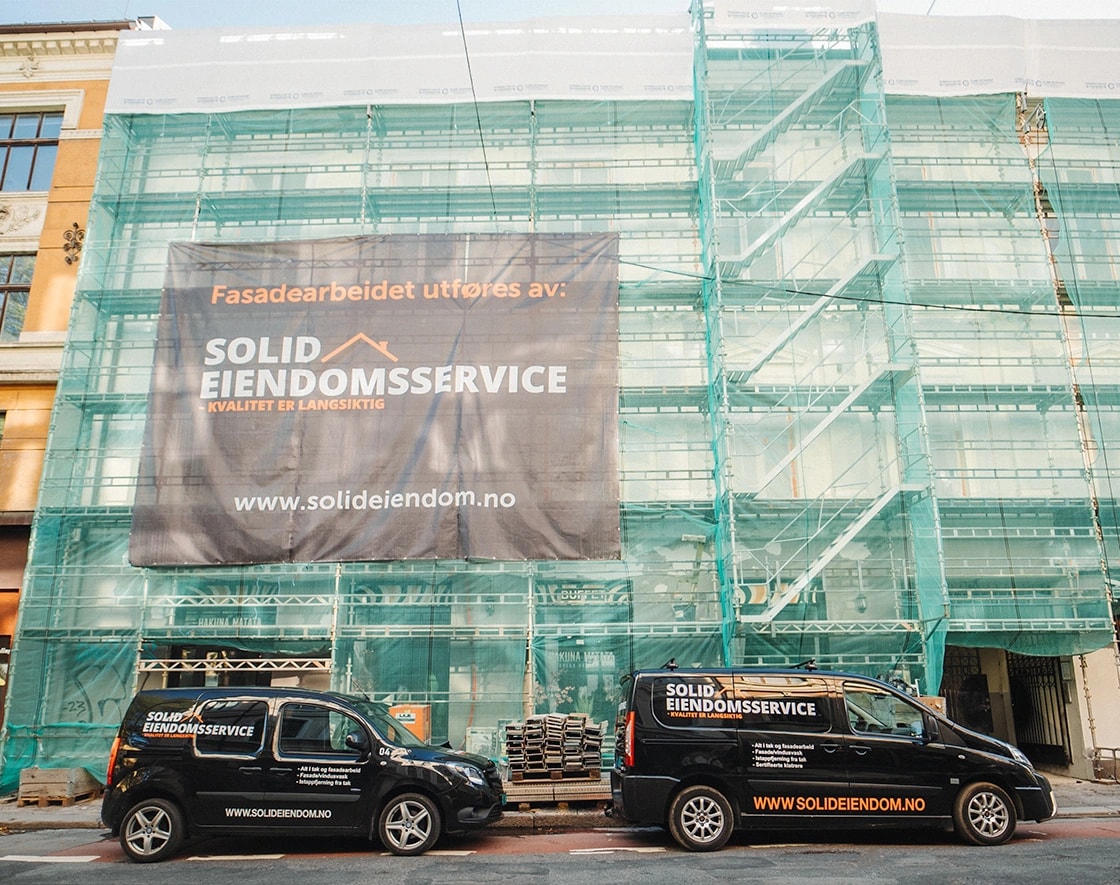 Stillas med Solid Eiendomsservice-banner og servicebiler foran bygården