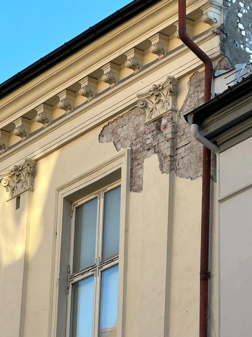 Bygårdsfasade med synlig tegl under puss og dekorerte vindusomramminger