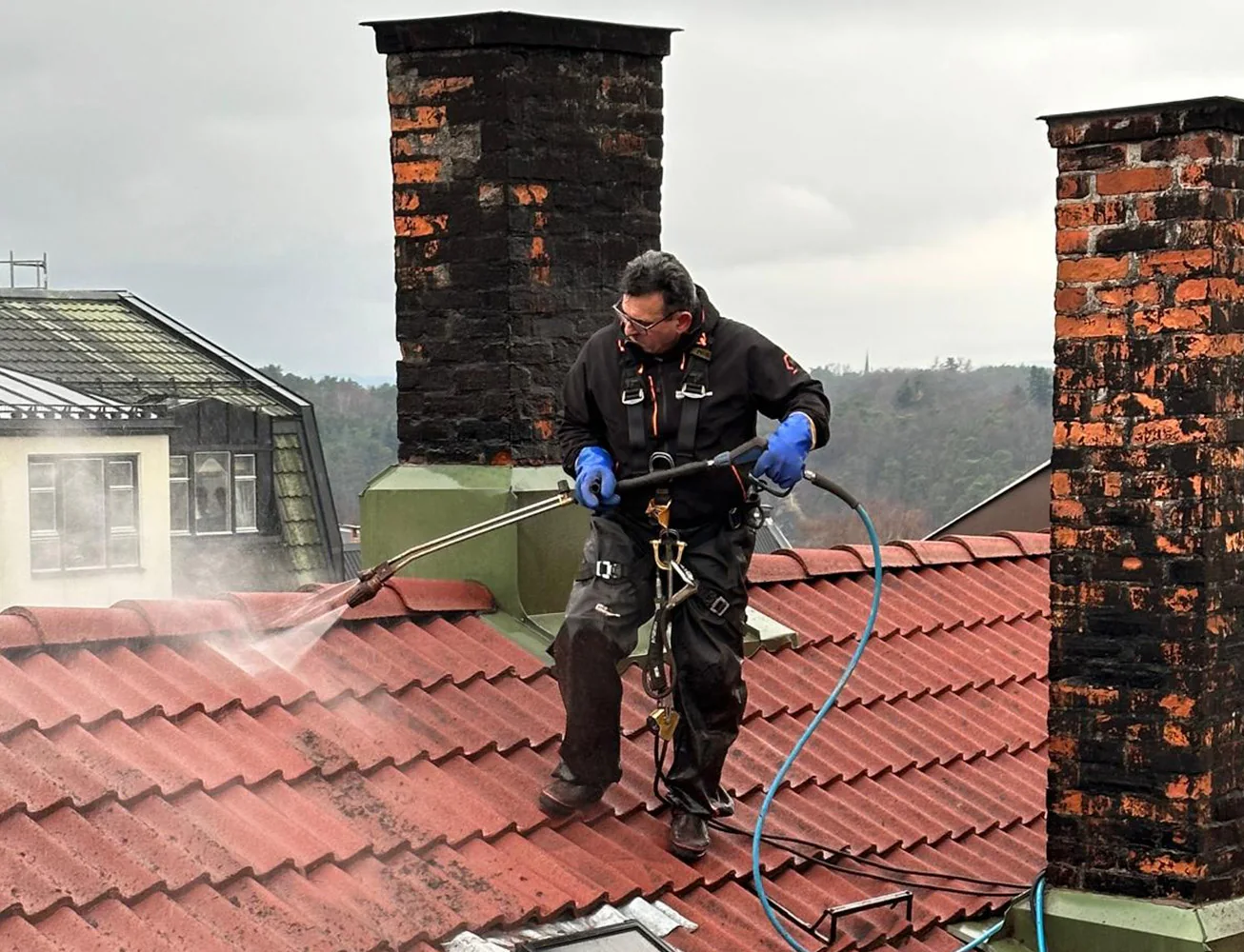 Arbeider med vaskeutstyr på rødt tak mellom to piper